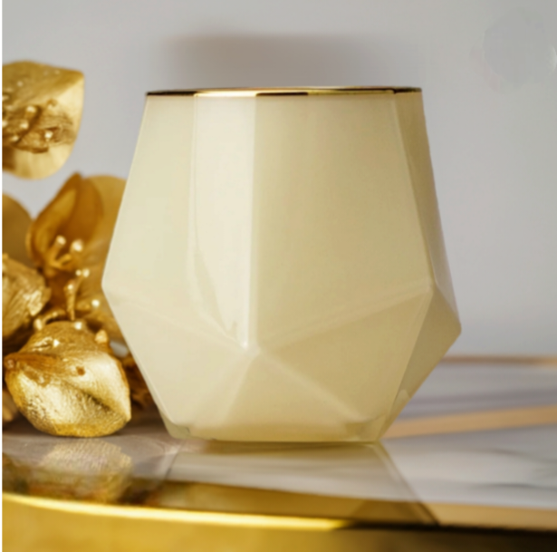 Gold geometric candle jar on a gold marble platform next to gold flowering branches