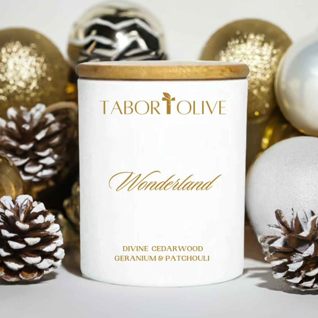 White candle jar with bamboo lid surrounded by gold and white Christmas decorations with gold text that says, "Wonderland. Divine cedarwood geranium and patchouli"