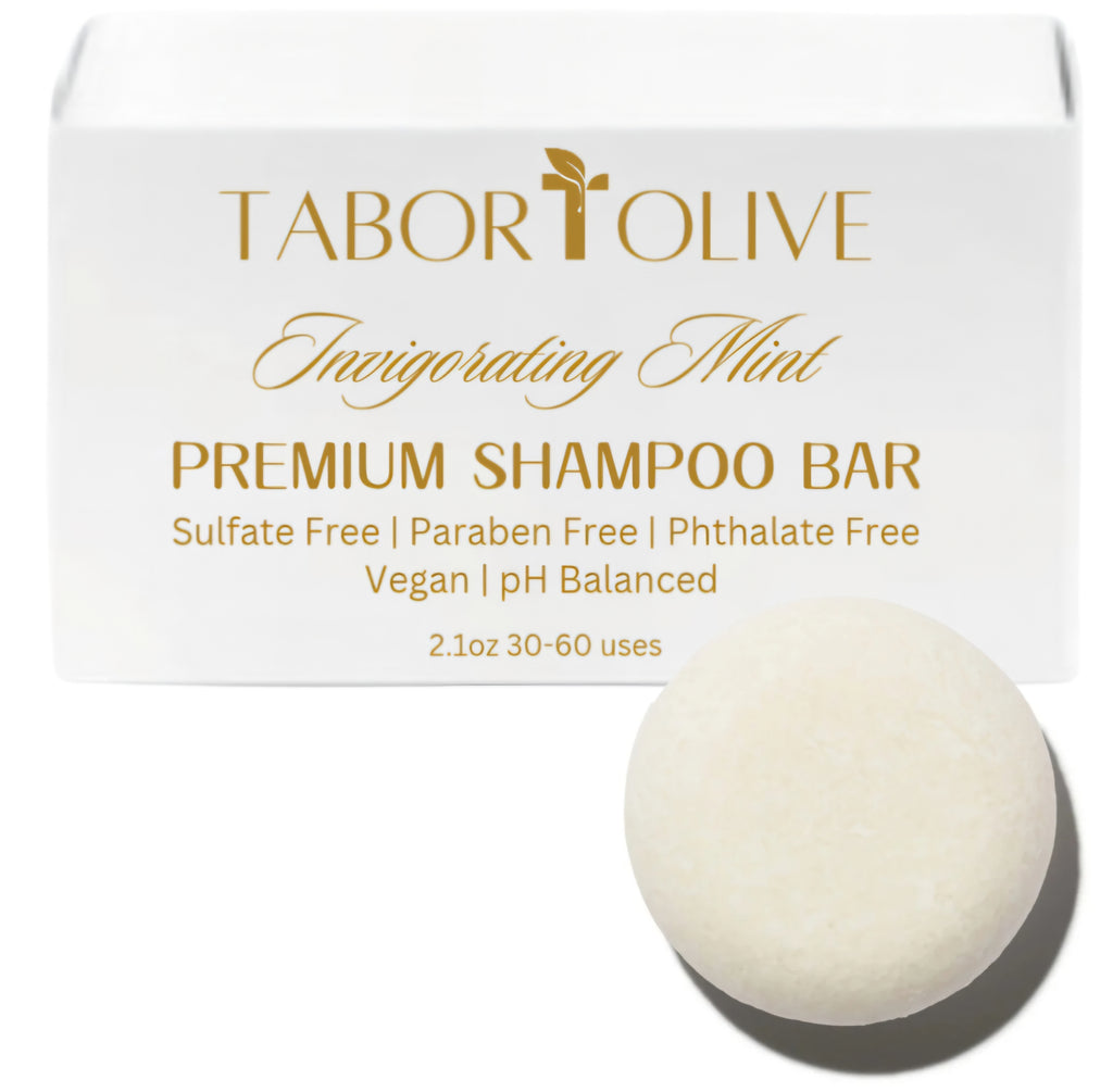 White soap box next to round shampoo bar with gold text that says, "invigorating mint shampoo bar. Sulfate free, paraben free, phthalate free, vegan, ph balanced"