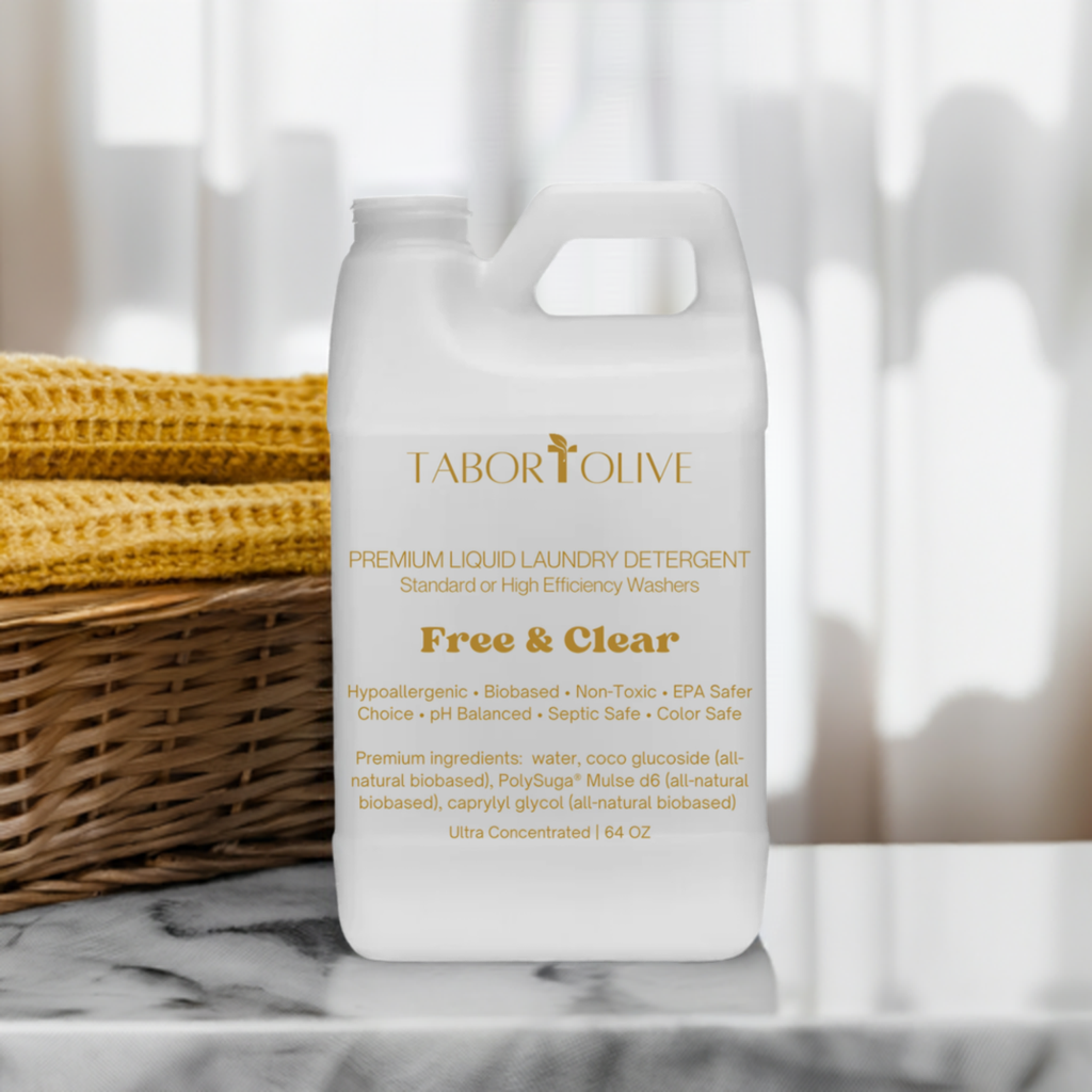 White detergent jug sitting on marble platform next to wooven basket with rust colorwd towels and gold text that says, "free and clear premium laundry detergent all natural hypoallergenic pH balanced non-toxic biobased preferred"